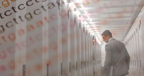 Businessman inspecting server racks with laptop and code overlay in data center corridor