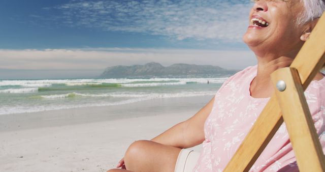 Senior woman sitting in a beach chair, smiling and relaxing on a sunny beach. Ideal for concepts of leisure, retirement, travel, and well-being.