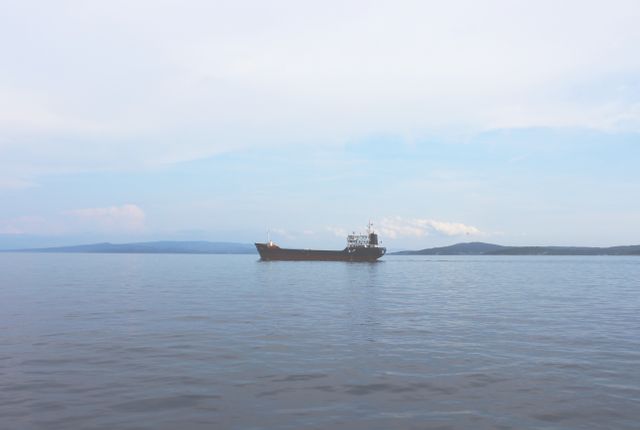 Cargo ship navigating calm sea under a clear sky. Could be used for illustrating maritime transport, ocean freight shipping, or depicting serene seascapes. Ideal for articles on shipping logistics, maritime industry, or tranquility and ocean views.