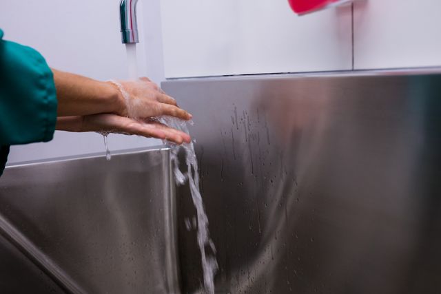 Surgeon washing hands under running water in a hospital setting, emphasizing hygiene and cleanliness. Useful for illustrating medical practices, healthcare hygiene protocols, and infection control measures in medical environments.