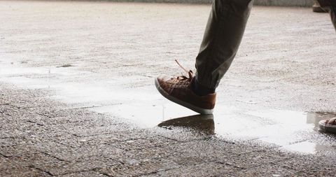 Mature man stepping through puddle on wet urban pavement with brown sneakers