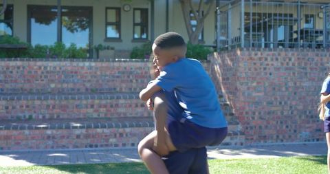 African american schoolboys playing piggyback in sunny schoolyard during recess