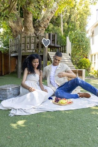 African american couple enjoying backyard picnic on blanket under treehouse with fruit board
