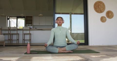 Asian woman meditating on patio wearing headphones and activewear for outdoor yoga