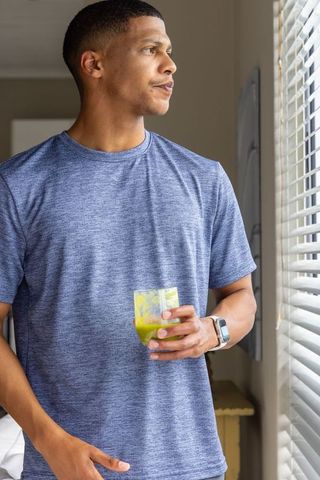 Contemplative african american man by window holding green juice wearing smartwatch
