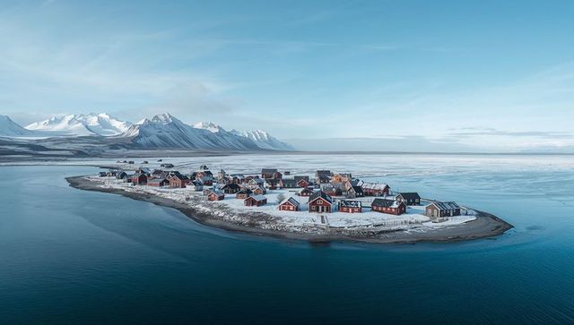 Snow-dusted arctic islet featuring red wooden cabins nestling in calm frozen bay