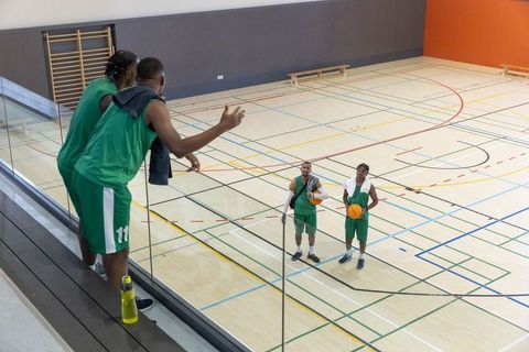 Diverse basketball team practicing on indoor court with teammates communicating from balcony