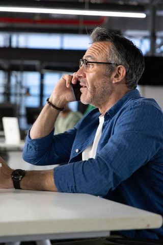 Middle-aged professional speaking on smartphone at modern open-plan coworking desk