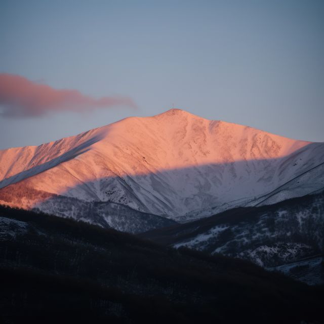 Sunset bathes a snowy mountain peak in warm light. The scene captures the tranquil beauty of nature as day transitions to night.