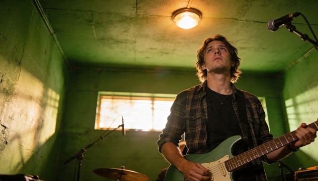Moody male guitarist rehearsing with seafoam electric guitar in green basement studio