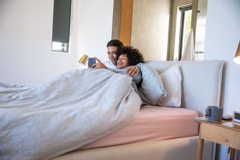 Diverse Male Partners Relaxing Together with Smartphone in Cozy Bedroom