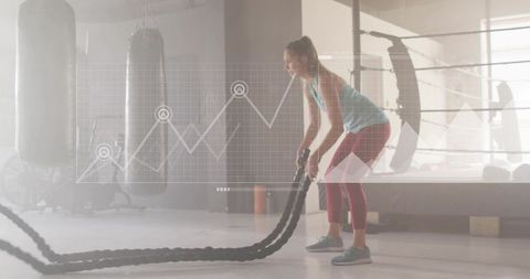 Female athlete swinging battle ropes in gym with performance graph overlay for fitness