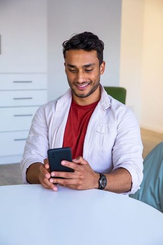 Young Asian Man Engaging with Smartphone at Home Office