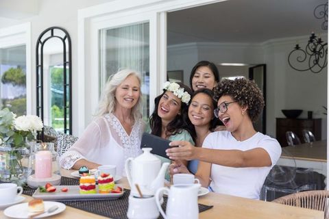 Multigenerational diverse women taking selfie at brunch table with tea cakes and flowers