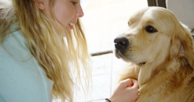 Happy caucasian female teenager petting her big dog with blond hair at home. Domestic life, pets, animals and care, unaltered.