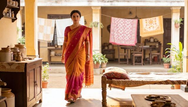 Sunlit indian woman walking in silk saree across old courtyard with charpoy
