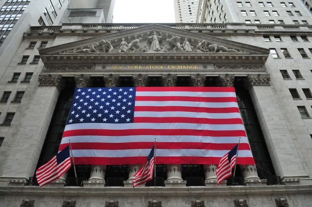 View showing large American flag covering facade of New York Stock Exchange in Manhattan's business district. Capture highlights iconic building in financial world, regularly used in content related to American economy, finance, investment, and national pride. Suitable for news articles, illustrative purposes, presentations, and educational materials concerning finance and stock market.