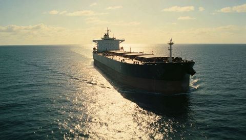 Ocean bulk carrier sailing at sunset with dark hull, bridge silhouette and glittering wake