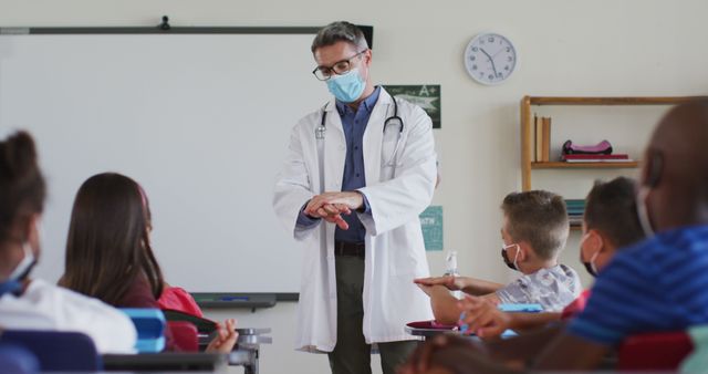 Diverse teacher disinfecting hands in classroom, with schoolchildren sitting wearing face masks - Download Free Stock Photos Pikwizard.com
