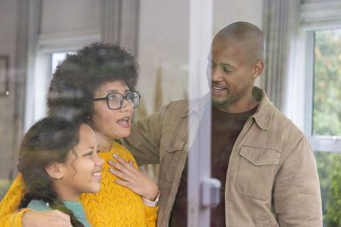 Cozy family embracing behind glass door smiling together at home in warm candid moment