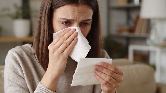 Woman holding and inspecting tissue on sofa showing cold symptoms and emotional discomfort