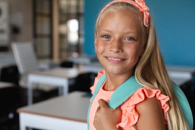 Portrait of smiling caucasian elementary schoolgirl with blond hair sitting in classroom. unaltered, childhood, education, playful and school concept.