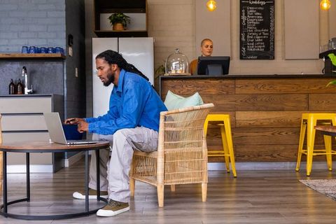 African american man working remotely on laptop in cozy cafe with rattan chair