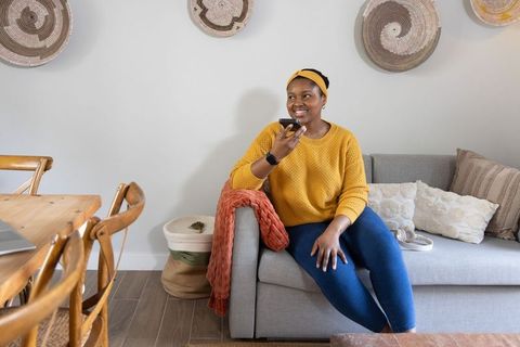 African american woman relaxing on sofa speaking into smartphone in cozy boho living room