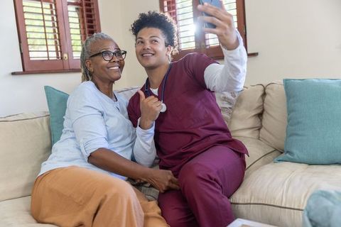 African american senior woman and caregiver taking selfie sharing warm bond and home care support