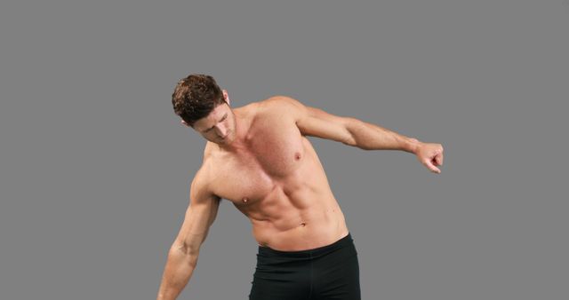 Fit man performing dynamic stretching exercise shirtless on a gray background. Useful for fitness and health-related content, exercise demonstrations, workout routines, sports training tips, and promotional materials for gyms and fitness programs.