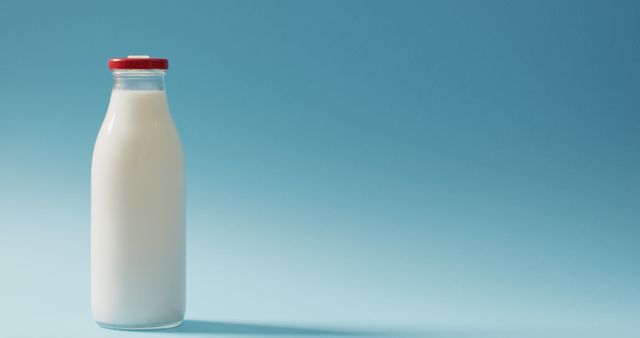 Simple glass bottle filled with milk against a blue background. Ideal for illustrating concepts related to dairy products, freshness, minimalism, and healthy beverages. Perfect for advertisements, product displays, and health campaigns.