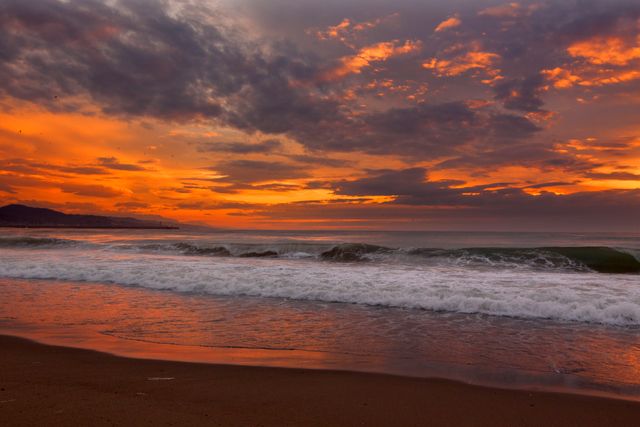 Dramatic sunset sky with orange and purple hues reflecting off ocean waves and wet sandy beach. Calm ocean scene ideal for travel brochures, blogs, and nature websites. Perfect for emphasizing tranquility, beauty of nature, and seaside destinations.