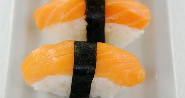 Two pieces of salmon nigiri sushi are presented on a white plate, with copy space. Sushi is a traditional Japanese dish consisting of vinegared rice topped with various ingredients, in this case, fresh salmon.