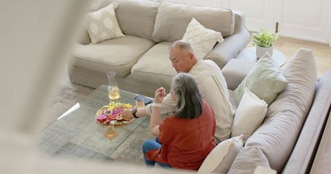 Senior asian couple sharing fruit and phone on cozy living room sofa with modern decor