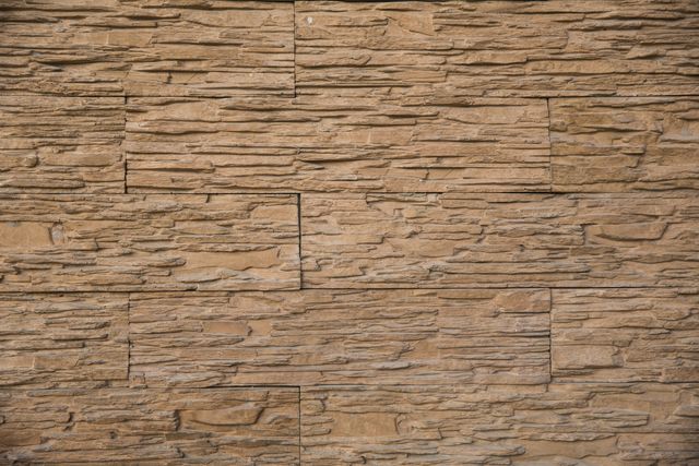 Detailed close-up image of a textured brown stone brick wall. Suitable for use in architectural designs, construction projects, landscape designs, presentations, or as a rustic background for text and graphic overlays. Ideal for showcasing natural materials and outdoor settings.