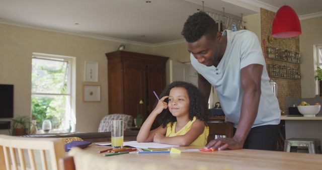 Father assisting daughter with homework in inviting kitchen. Ideal for educational, family bonding, and home study themes. Perfect for depicting supportive parenting, childhood education, or daily family life.