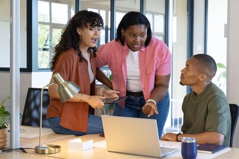 Diverse team collaborating around laptop and tablet in modern office workspace