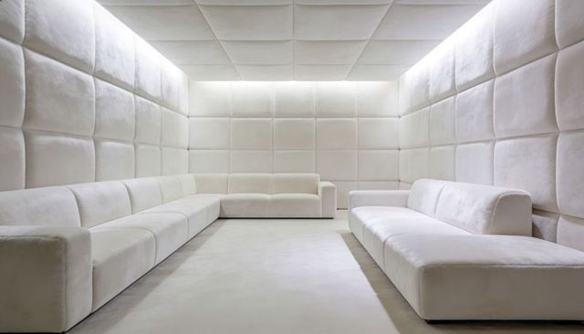 Minimal monochrome cream lounge with u-shaped sofas and quilted acoustic wall panels