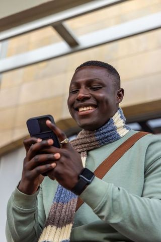 Smiling man texting on flip phone wearing smartwatch and knitted scarf, urban commuter