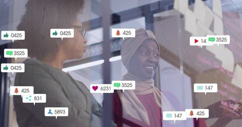 Black colleague wearing hijab collaborating at glass wall with social media notifications