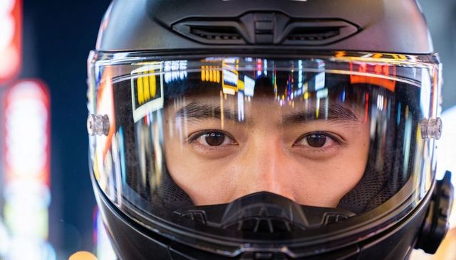 Rider peering through helmet visor reflecting neon city lights and urban night bokeh