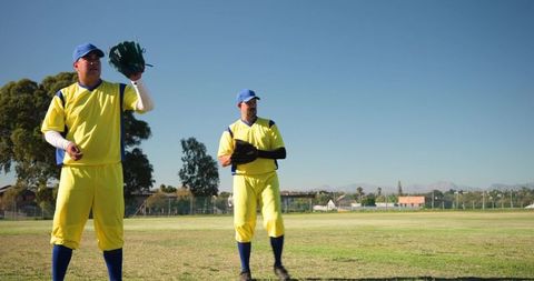 Two Baseball Players Standing in Outfield Holding Gloves and Ball Wearing Yellow Uniforms