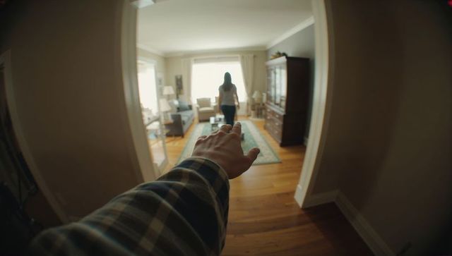 Reaching hand toward walking woman in backlit living room from hallway, first-person perspective