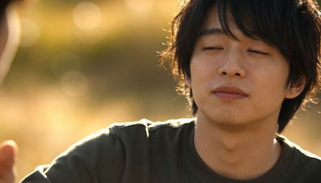 Asian young man relaxing in golden sunlight, eyes partly closed, warm rimlit headshot