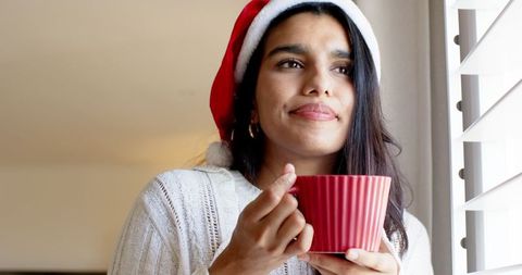 Festive Woman in Santa Hat Sipping a Drink by Window