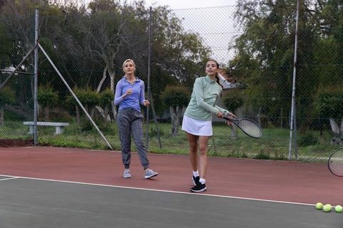 Women practicing tennis together on outdoor court in casual athleticwear and skirt