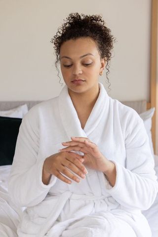 African american woman sitting in bed wearing white terry bathrobe checking fingers morning self car