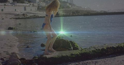 Woman exploring mossy shoreline in coastal village setting