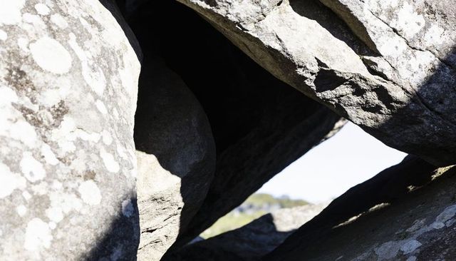 Sunlit interlocked boulders framing dark crevice with lichen-patched rock texture