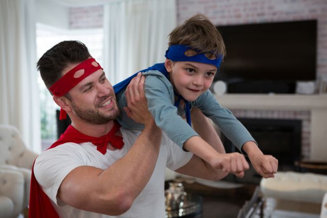 Father and son wearing superhero costumes enjoying playtime at home. Great for illustrating family bonding, parental love, and imaginative play. Ideal for parenting blogs, family activity websites, and advertisements promoting family-oriented products.